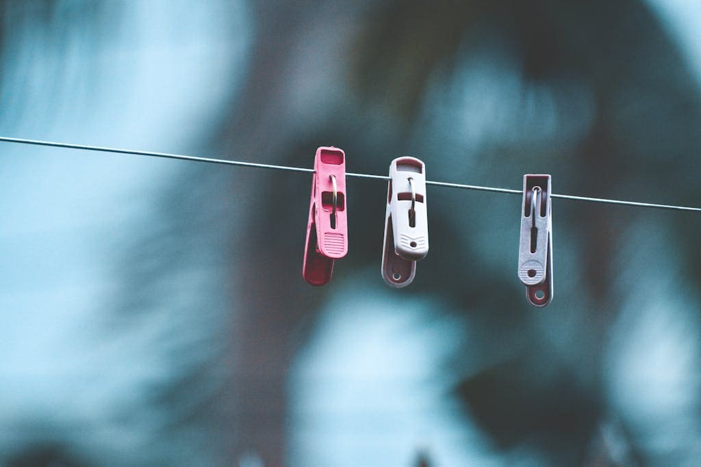 Close-up of three colorful clothespins on a wire with a blurred outdoor background.